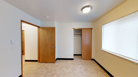 A room with a carpeted floor, a window with blinds, and a wooden door.