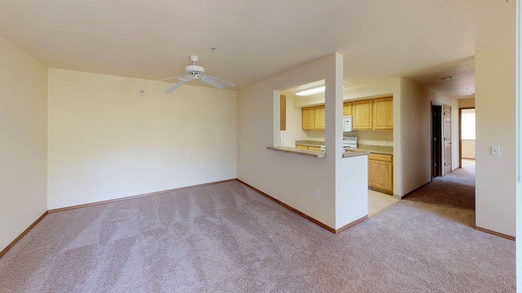 an empty living room with a ceiling fan and a kitchen