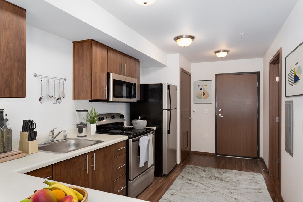a kitchen with stainless steel appliances and wooden cabinets and a door to a hallway
