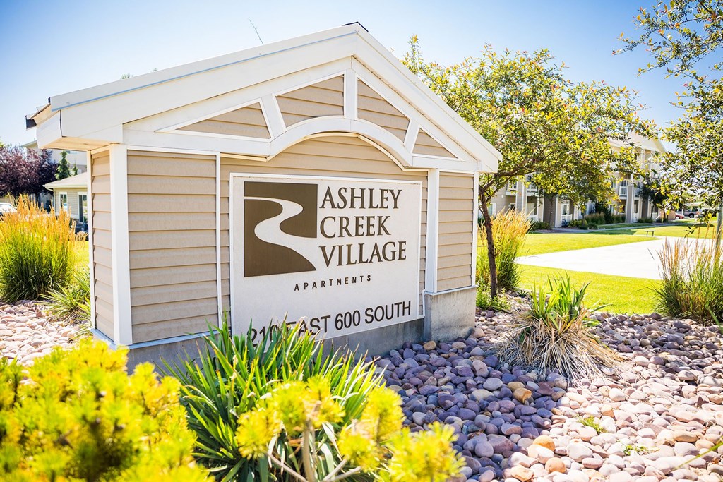 A sign for Ashley Creek Village Apartments is displayed in front of a landscaped area.