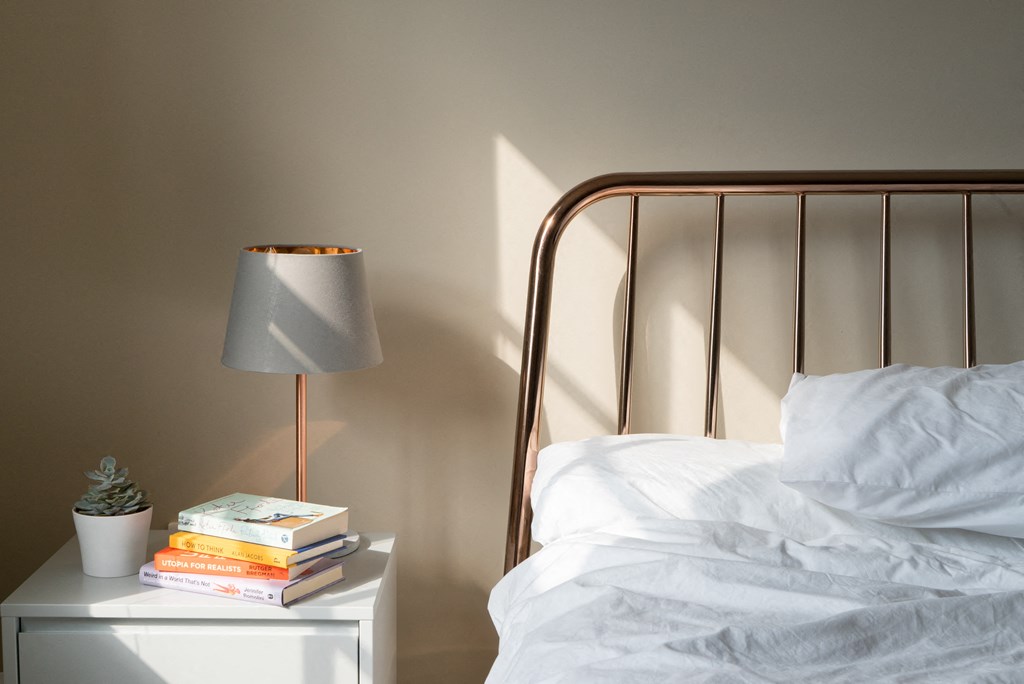 a bed with white sheets and a nightstand with a lamp and books