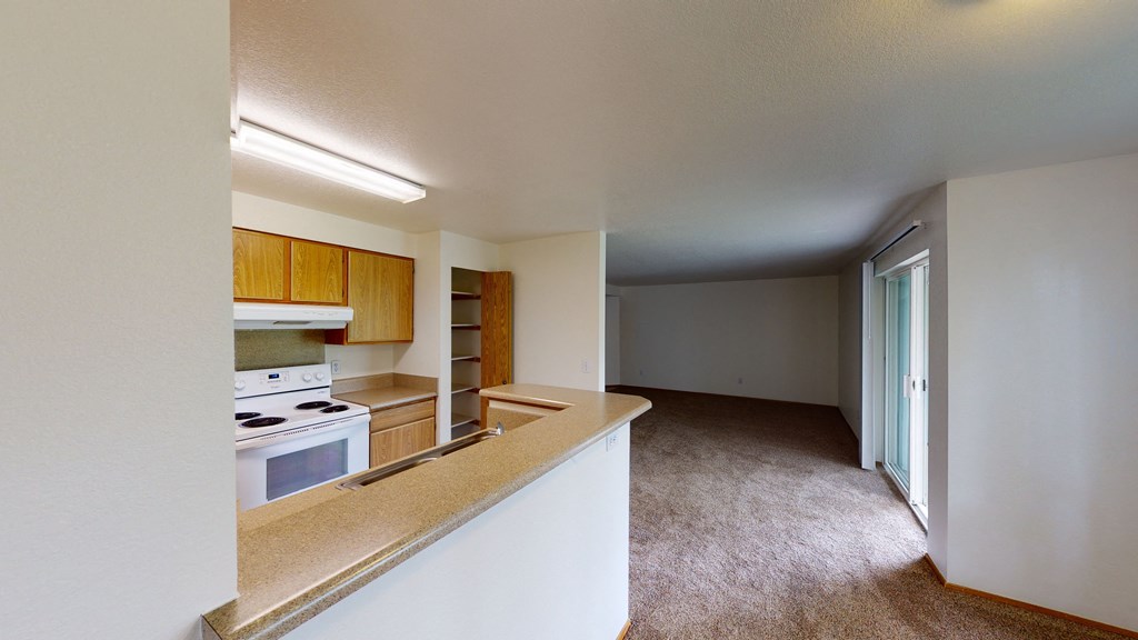 an empty kitchen with an empty living room in the background