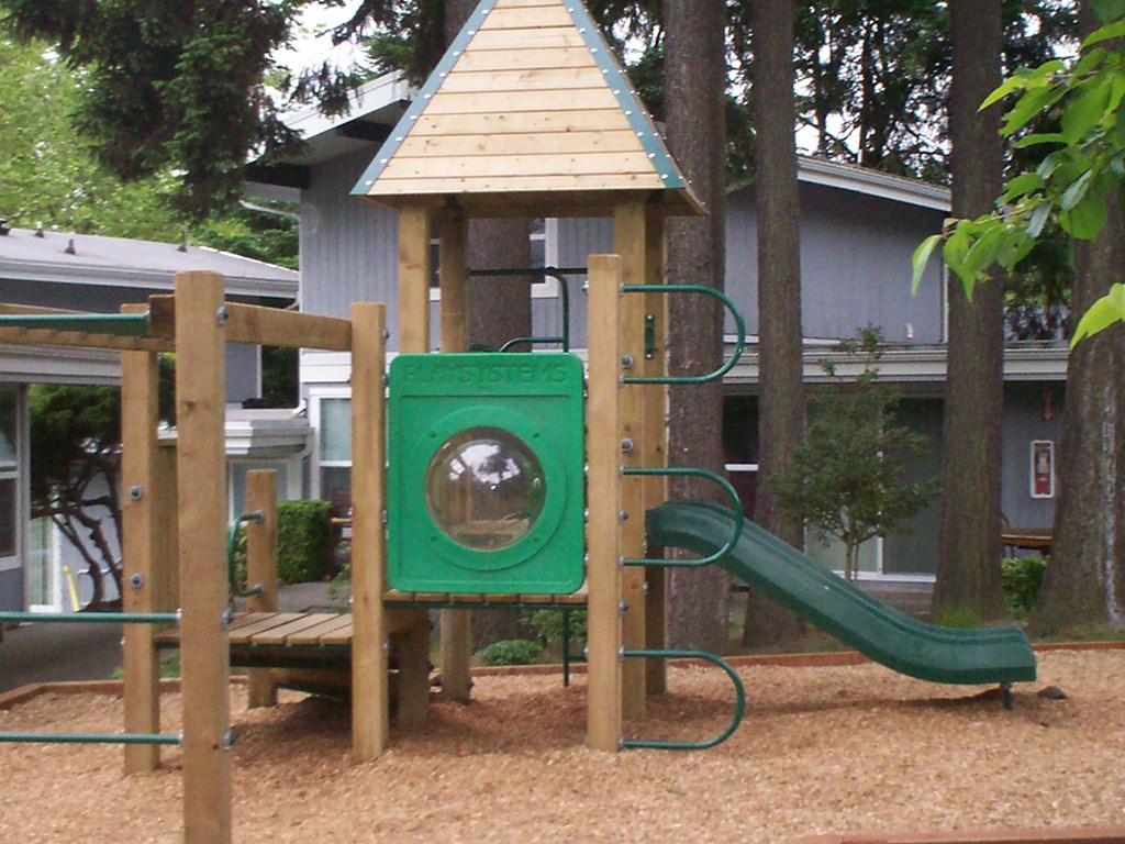 A playground with a green slide and a wooden structure.