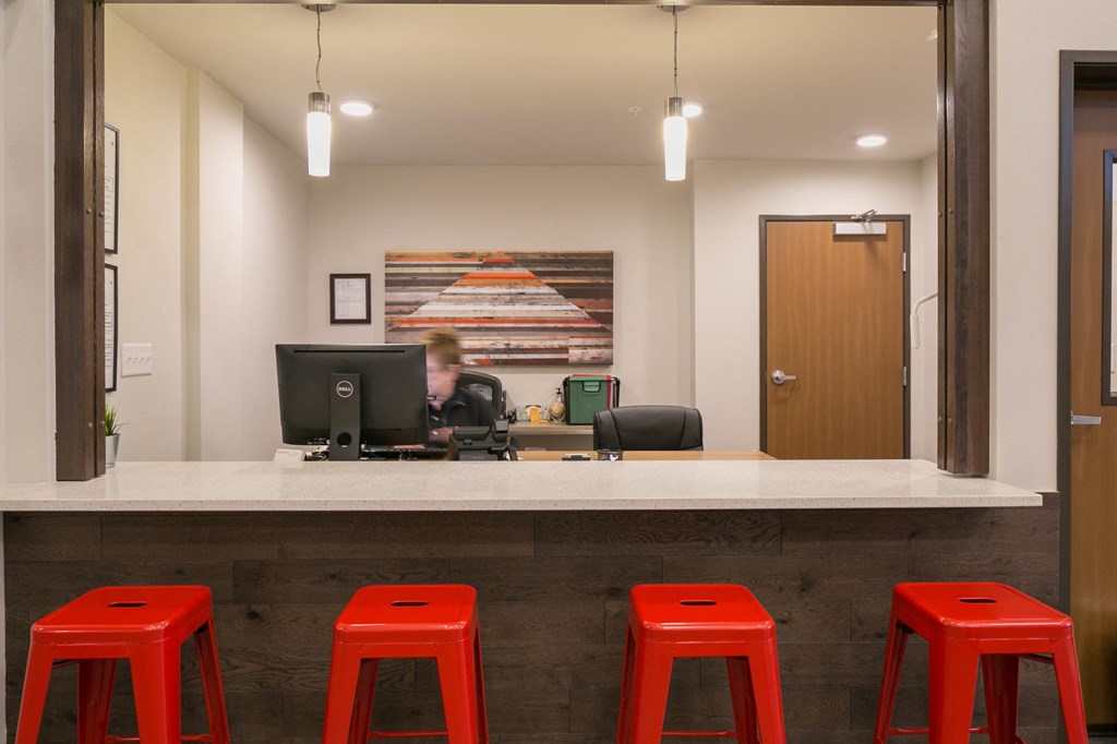 a bar with four red stools in front of a desk with a computer
