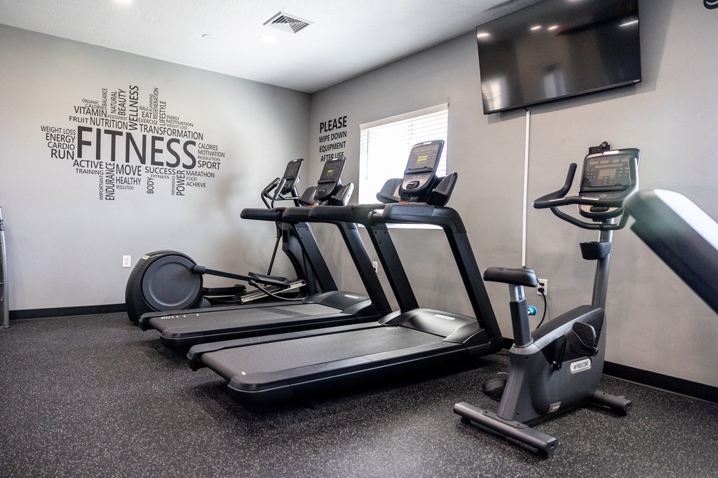 A fitness room with a treadmill, elliptical trainer and a wall with fitness related words.