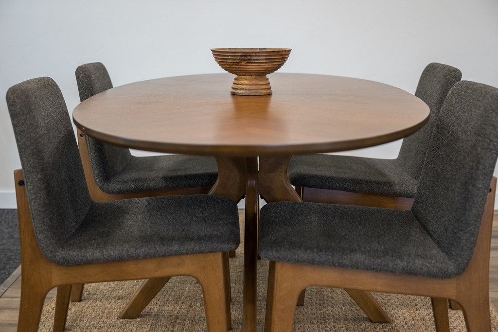 A wooden dining table with a pedestal base and four grey chairs.