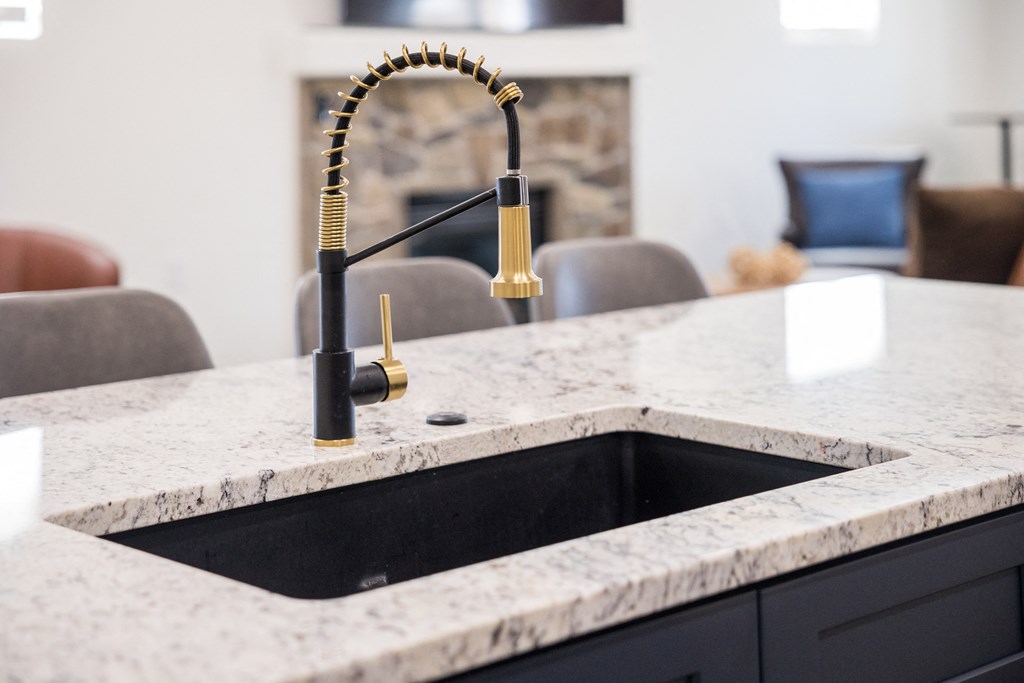 A kitchen sink with a marble countertop and a gold faucet.