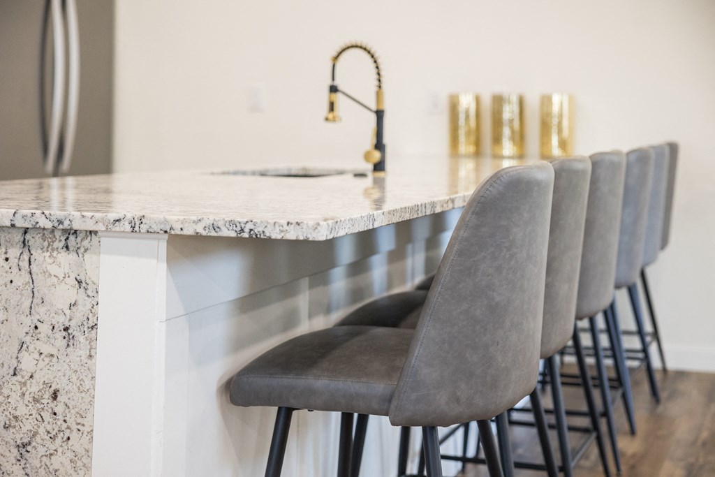 A row of grey bar stools are lined up in front of a marble counter.