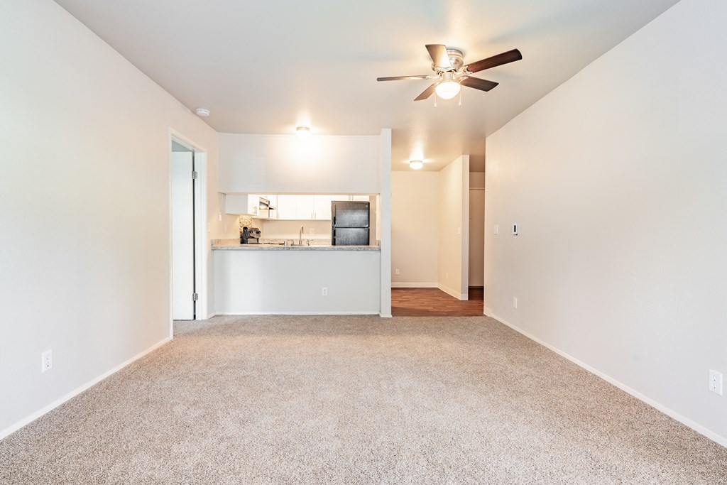 a living room with a ceiling fan and a kitchen in the background