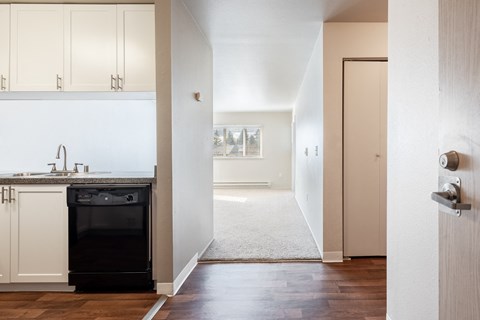 a kitchen with white cabinets and a black dishwasher and a hallway with a door