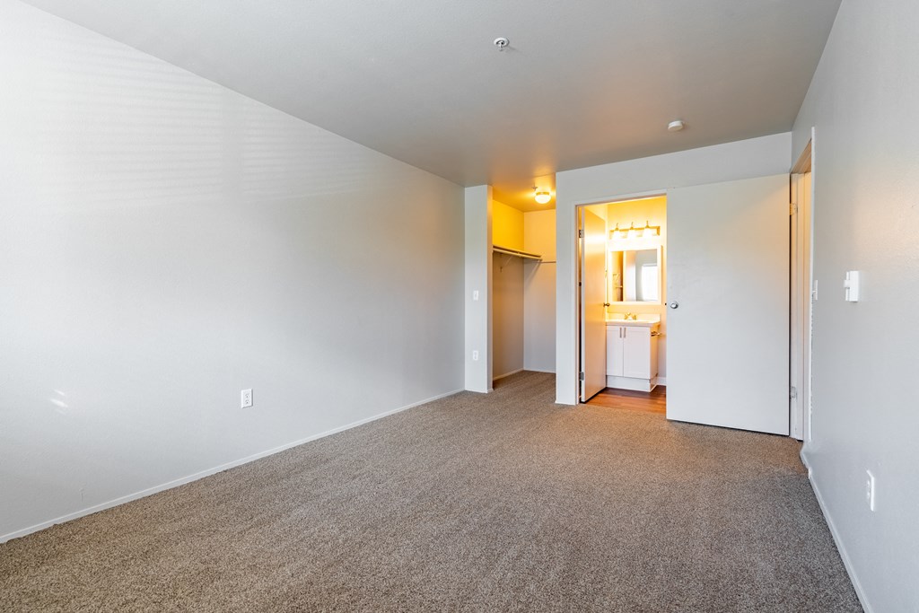 a bedroom with a carpeted floor and a bathroom in the background