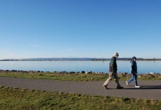 two people walking on a sidewalk near a body of water