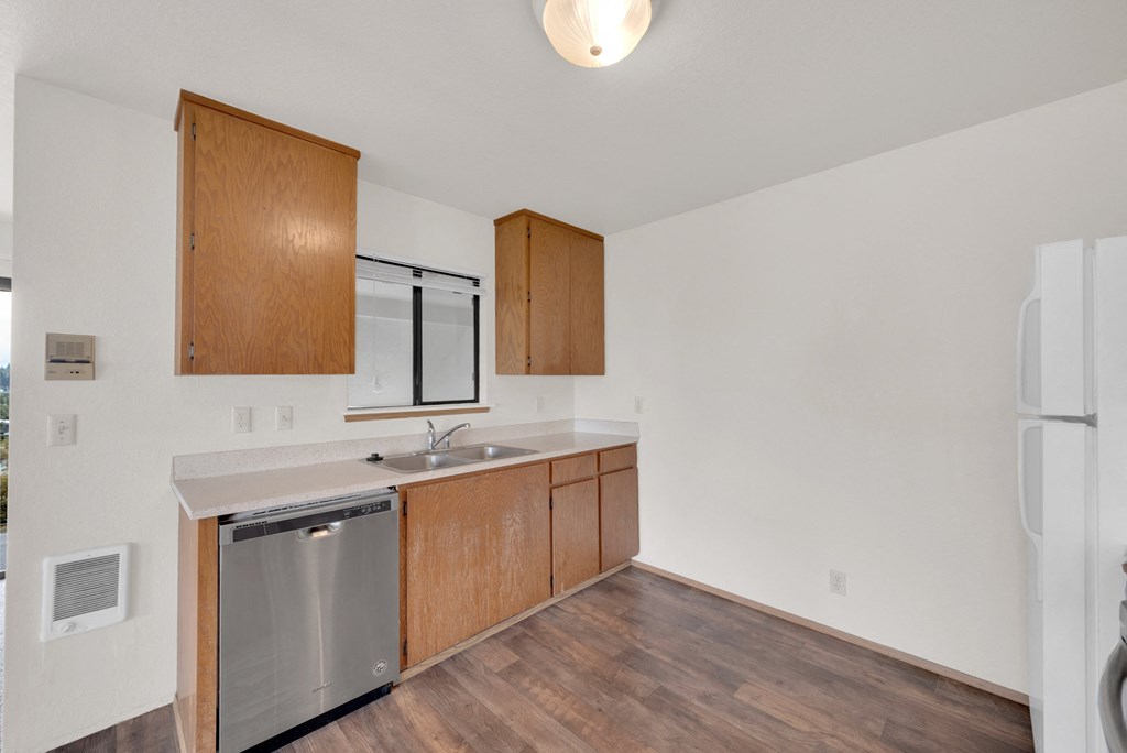 an empty kitchen with wooden cabinets and a stainless steel dishwasher