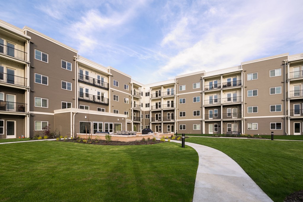 an exterior view of an apartment building with green grass and a sidewalk