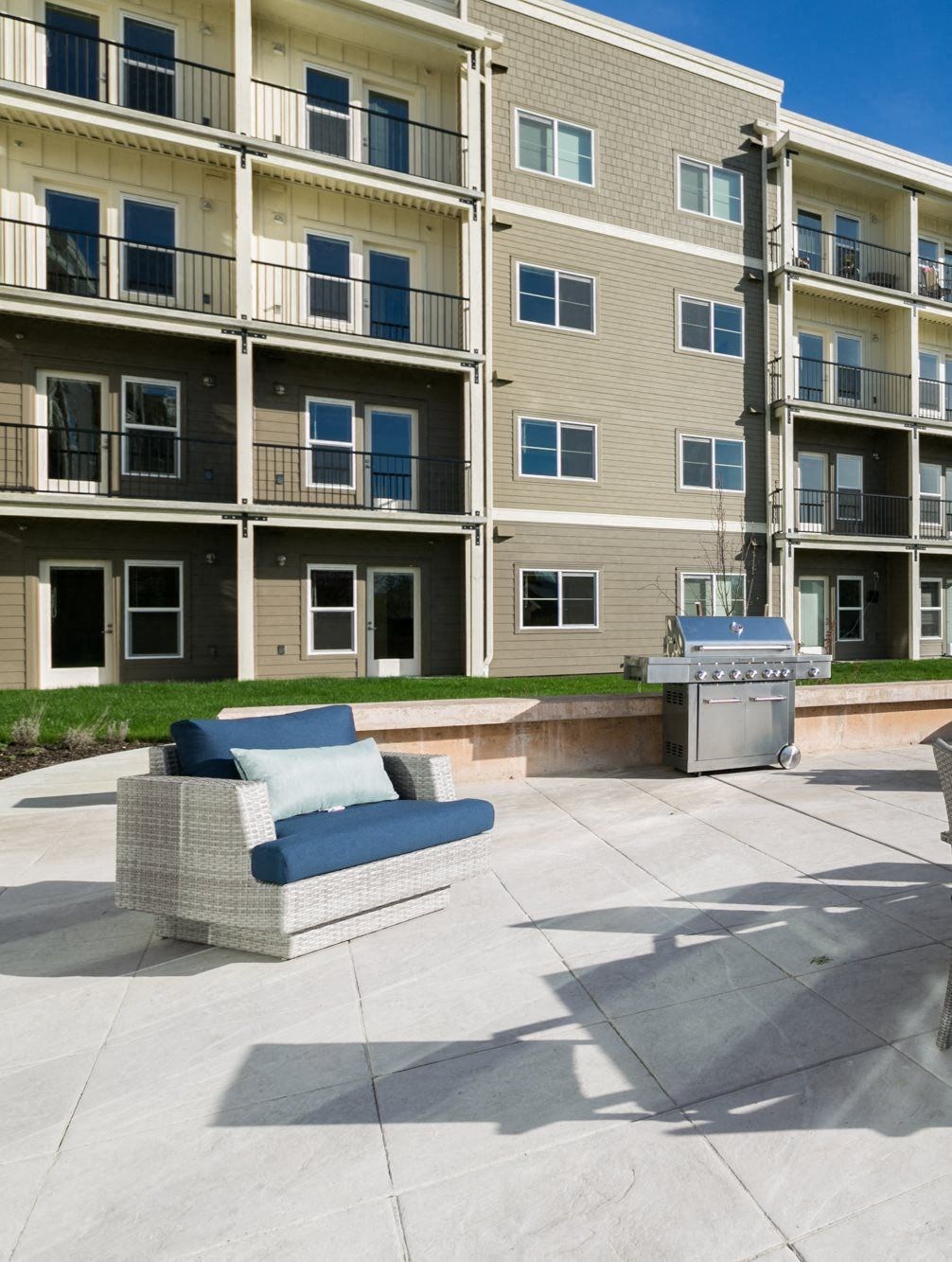 a patio with a couch and a grill in front of an apartment building