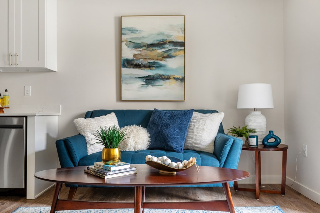 A living room with a blue couch and a painting on the wall.