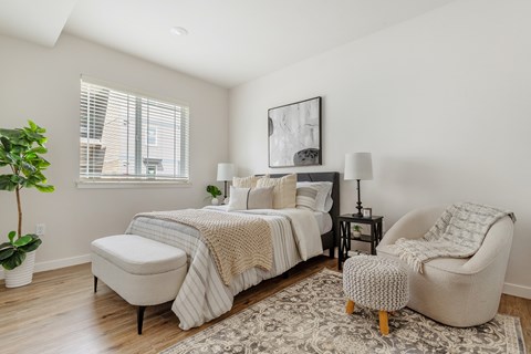 A bedroom with a large bed, a chair, and a potted plant.