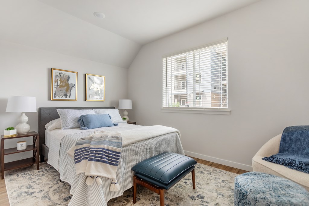 A bedroom with a bed, a chair, and two lamps.