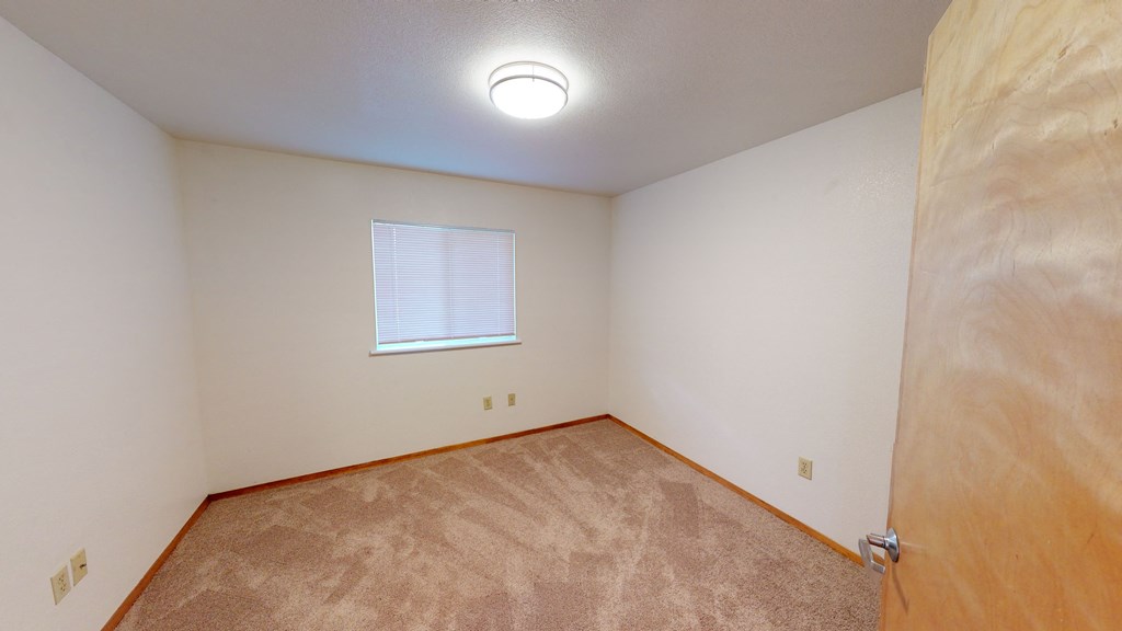 the living room of an empty home with a wooden door and a window