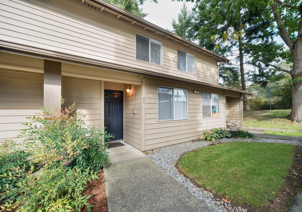 the front of a tan house with a sidewalk and a black door