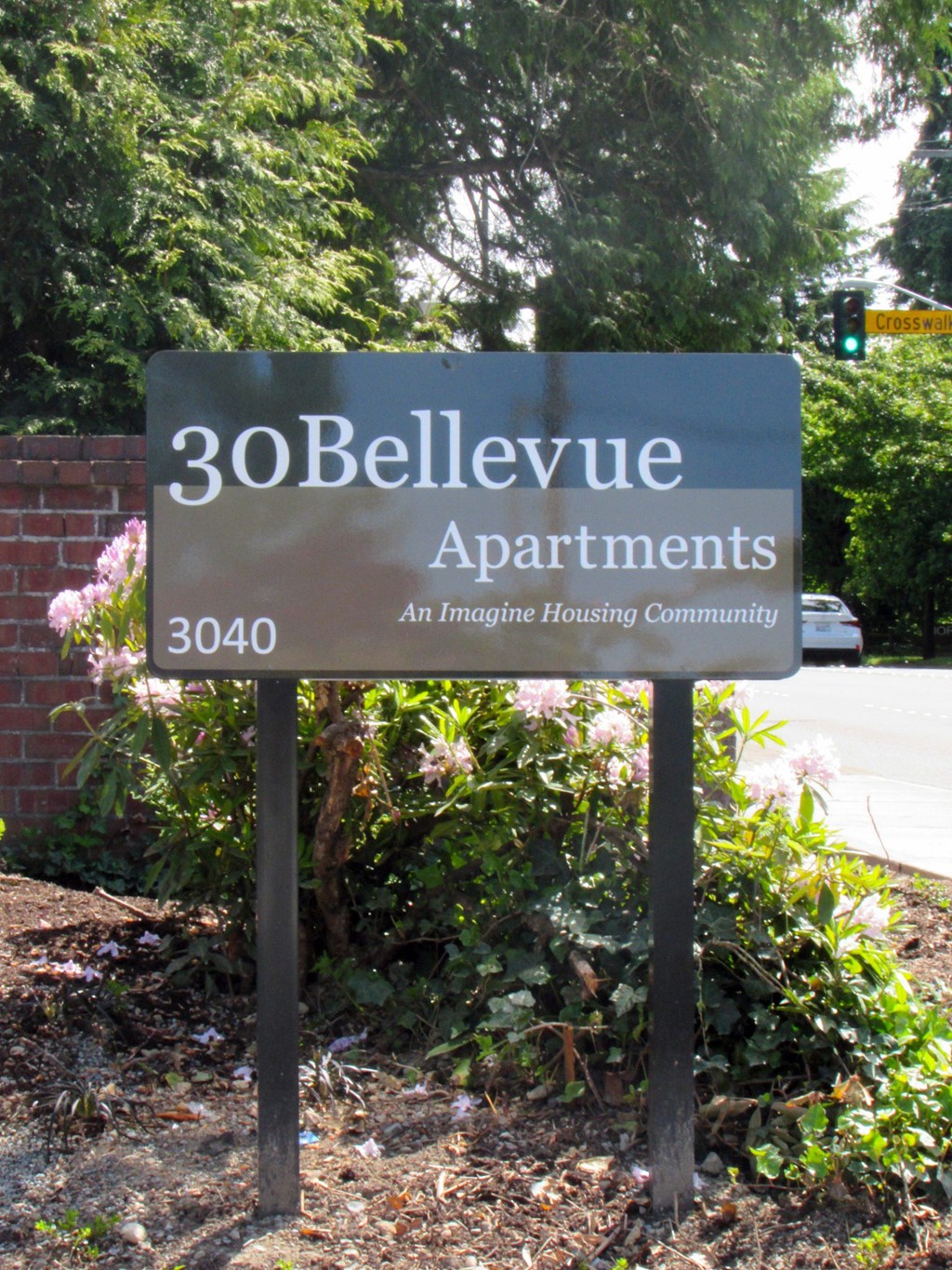 A sign for 30Bellevue Apartments stands in front of a brick wall and greenery.
