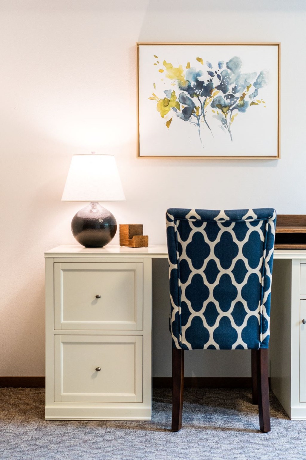 a desk with a chair and a lamp and a painting on the wall