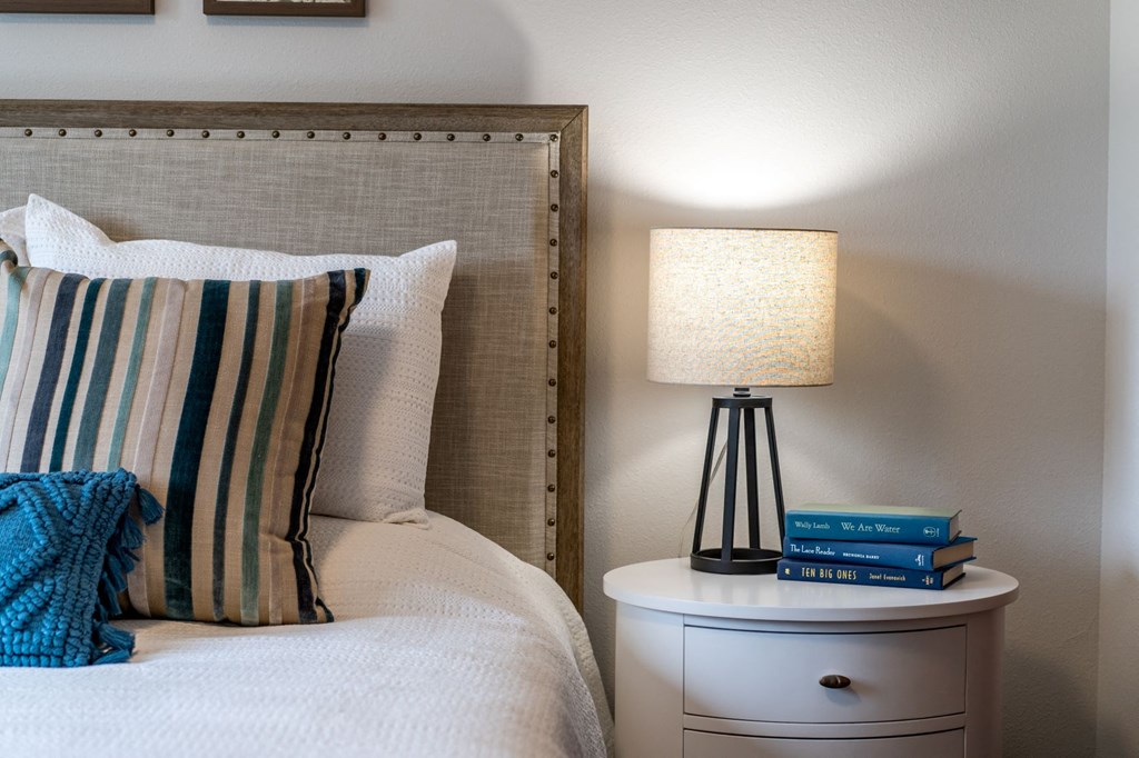 a bedroom with a bed and a nightstand with a lamp and books