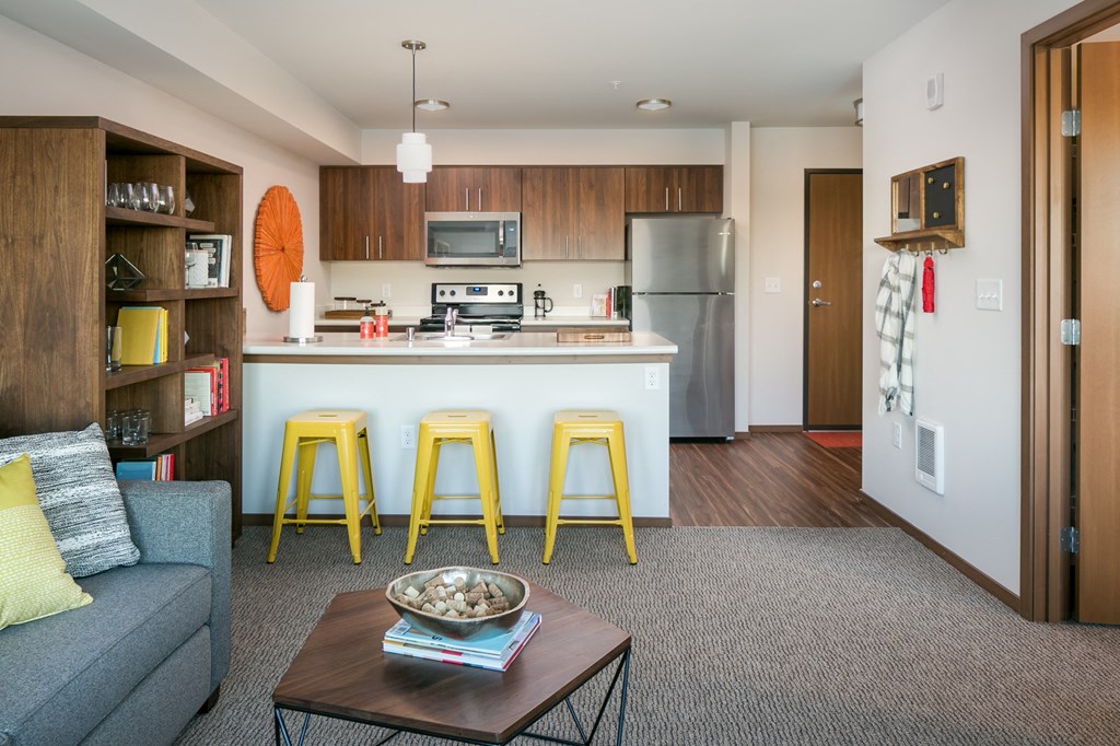 a living room with a kitchen with a bar and yellow stools