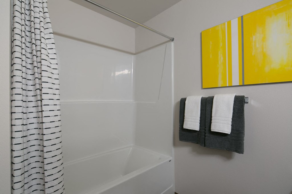 a small bathroom with a shower and a yellow painting on the wall