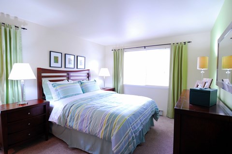 A bedroom with a bed, nightstands, and a window with green curtains.