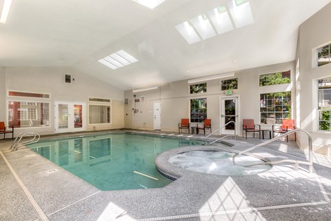 A large indoor swimming pool with a hot tub and lounge chairs.