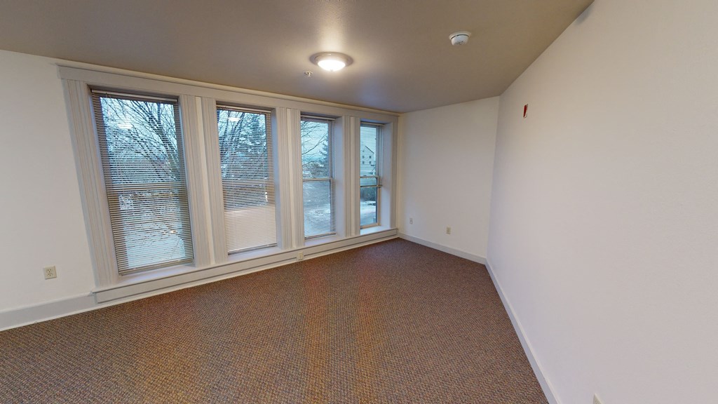 an empty living room with large windows and carpeting