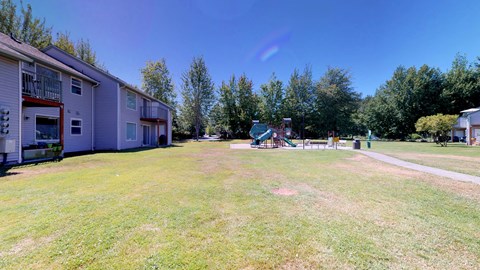 A sunny day at the park with a playground and apartment buildings in the background.