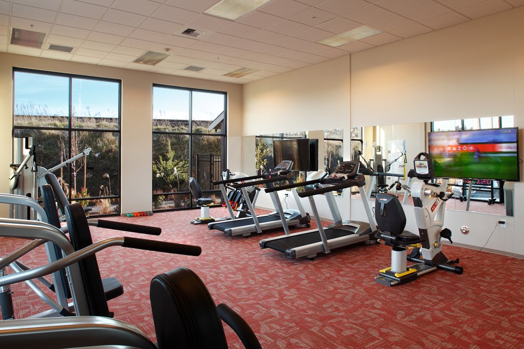 a gym with cardio equipment in a room with windows