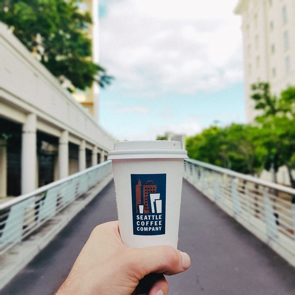 a hand holding a cup of coffee on a bridge