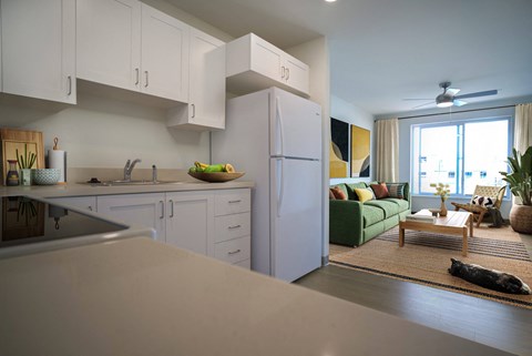 A kitchen with white cabinets and a green couch in the living room.
