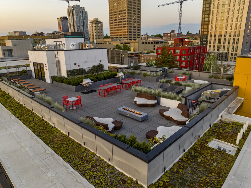 A rooftop patio with red chairs and tables overlooks a city skyline.