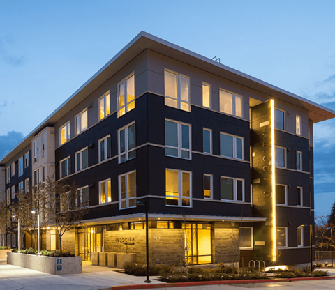 A modern building with a dark facade and lit windows.