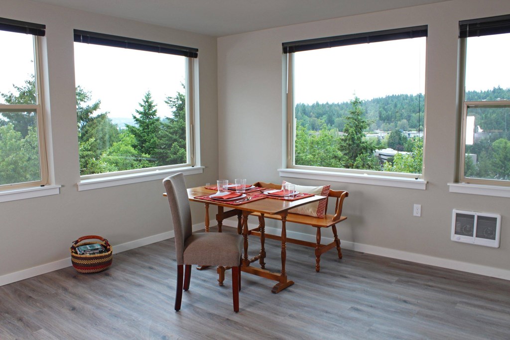 A dining room with a table set for two and a view of trees outside the window.