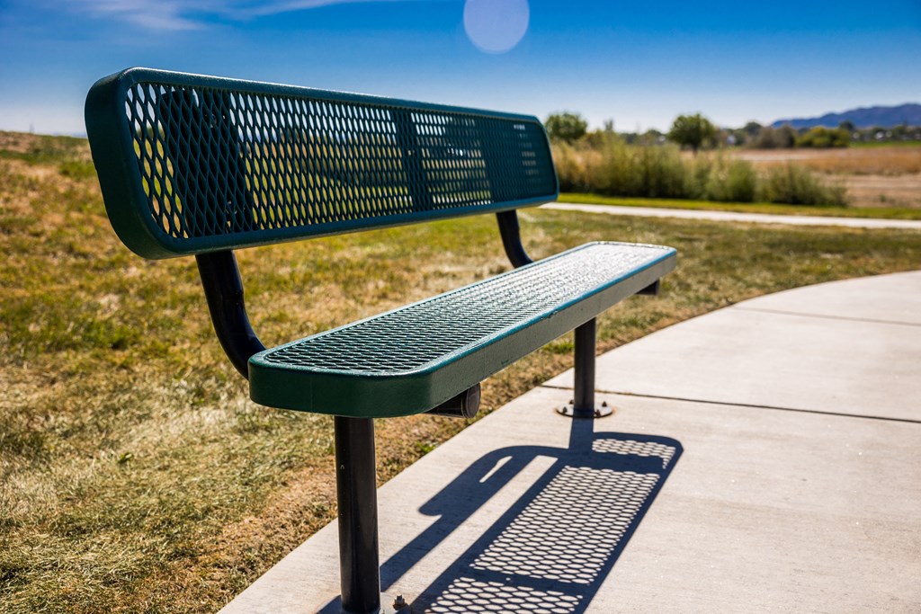 A green metal bench with a backrest and armrests sits on a concrete platform with a wheelchair symbol painted on the ground.
