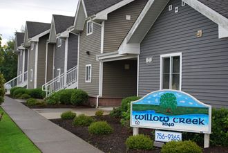 a building with grey siding and a blue and white sign that reads willow creek