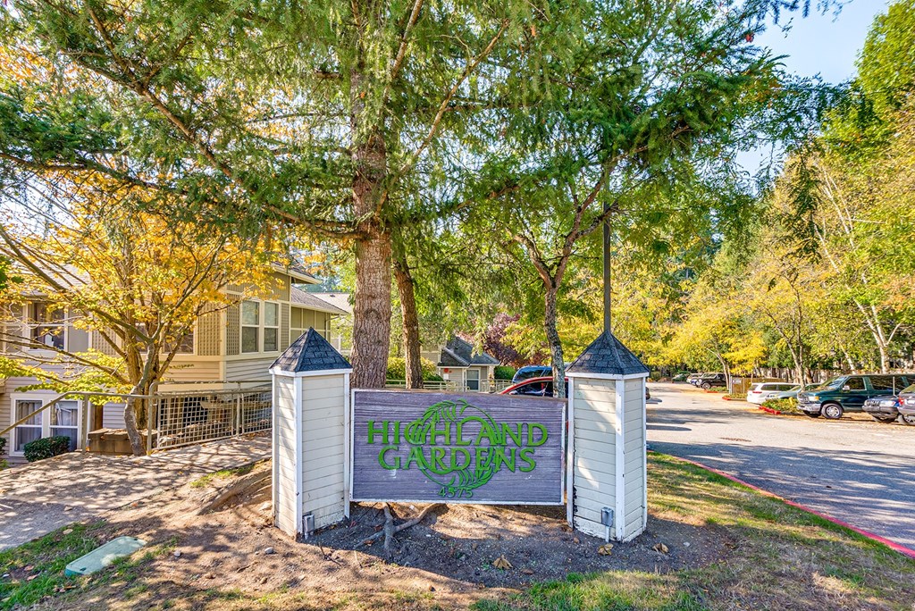 A sign that says "Hillcrest Gardens" is in front of a tree.