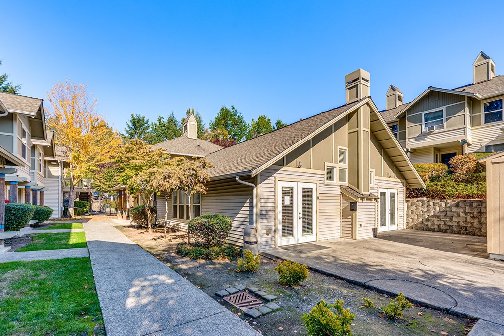 A house with a grey roof and a white door is surrounded by a green lawn.