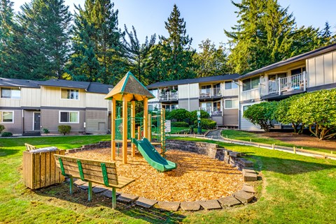 A playground with a green slide and a wooden bench.