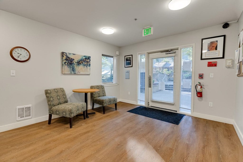 A room with a clock on the wall and two chairs with a table in between.