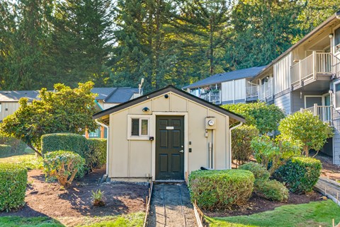 A small house with a green door is surrounded by bushes and trees.