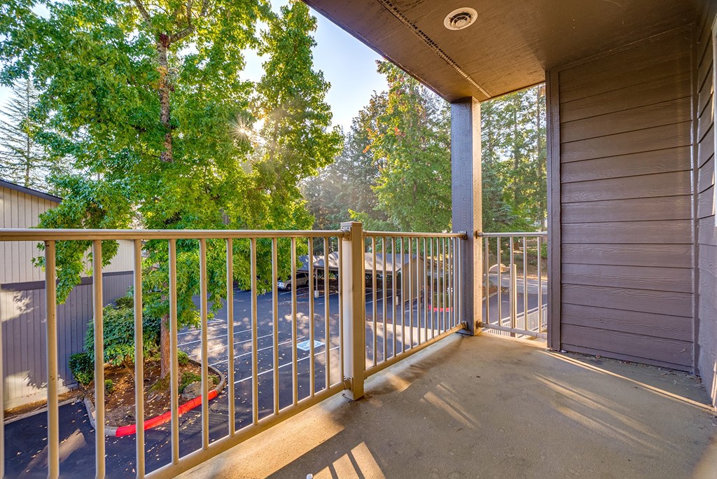 A balcony with a metal railing and a view of a parking lot and trees.