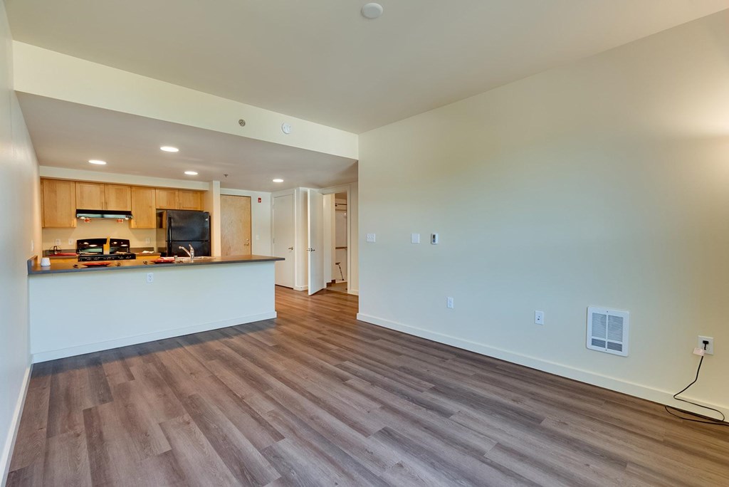 A spacious room with wooden flooring and a kitchen area with white countertops.