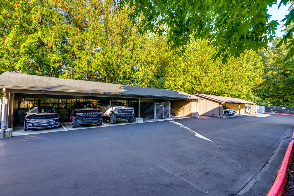 A parking lot with cars parked in front of a building with a roof and a fence.