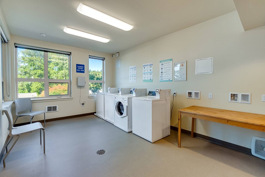 A laundry room with a washer and dryer, a chair, and a table.